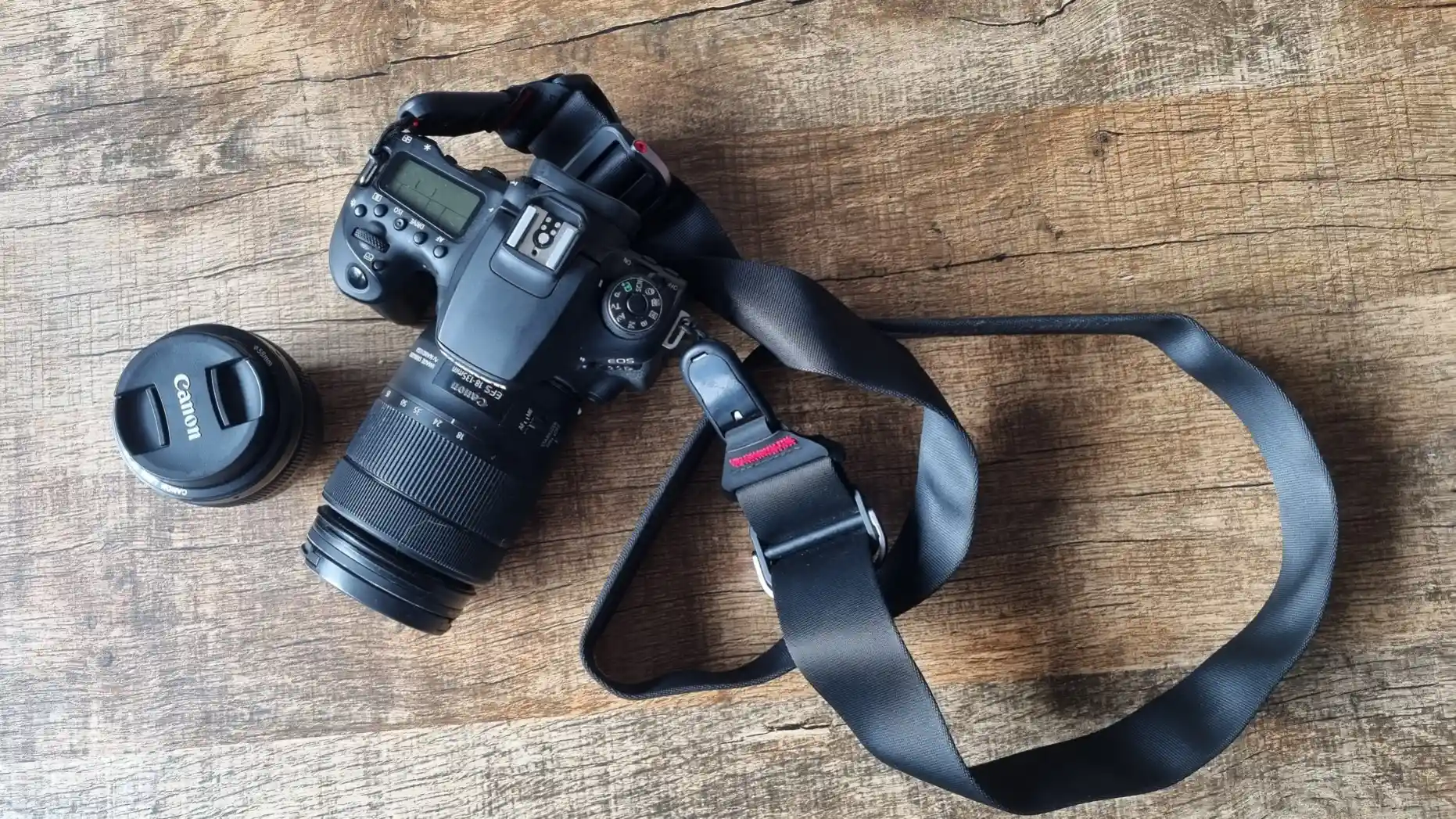 DSLR camera with lens and a wide camera strap, photographed from above.