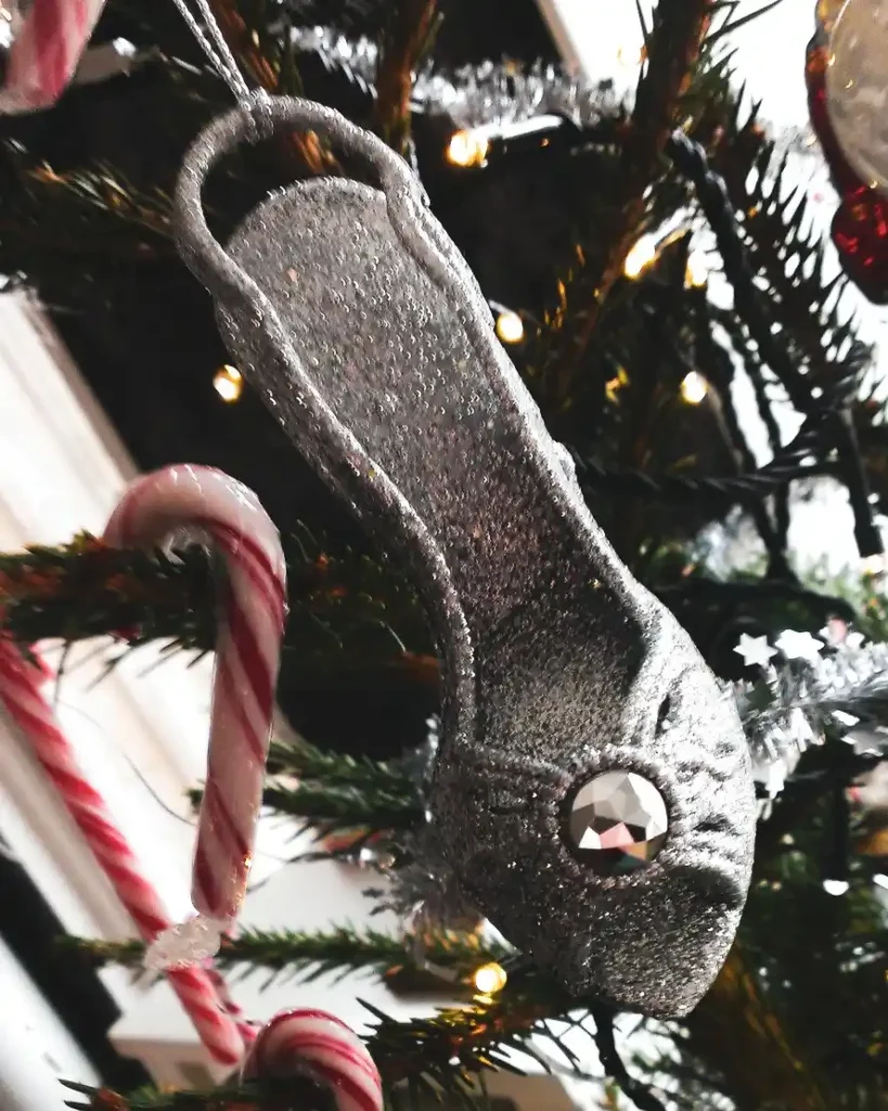 Silver high-heel Christmas ornament hanging among green fir branches.