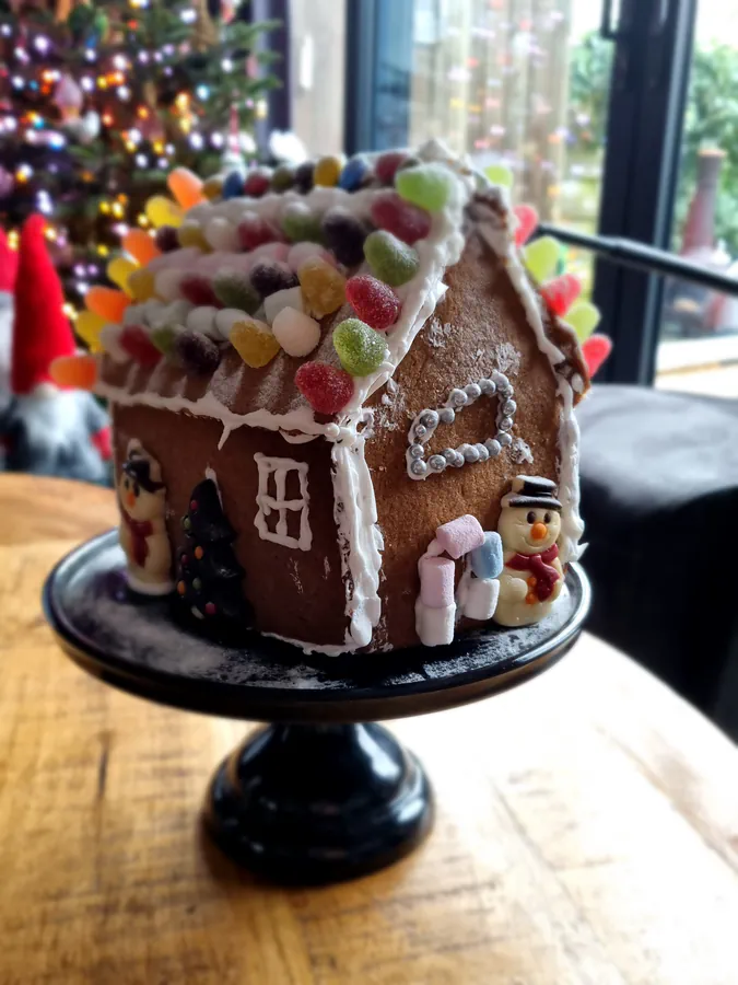 Real gingerbread house decorated with white icing, colourful sweets and a red-and-white striped candy arch.